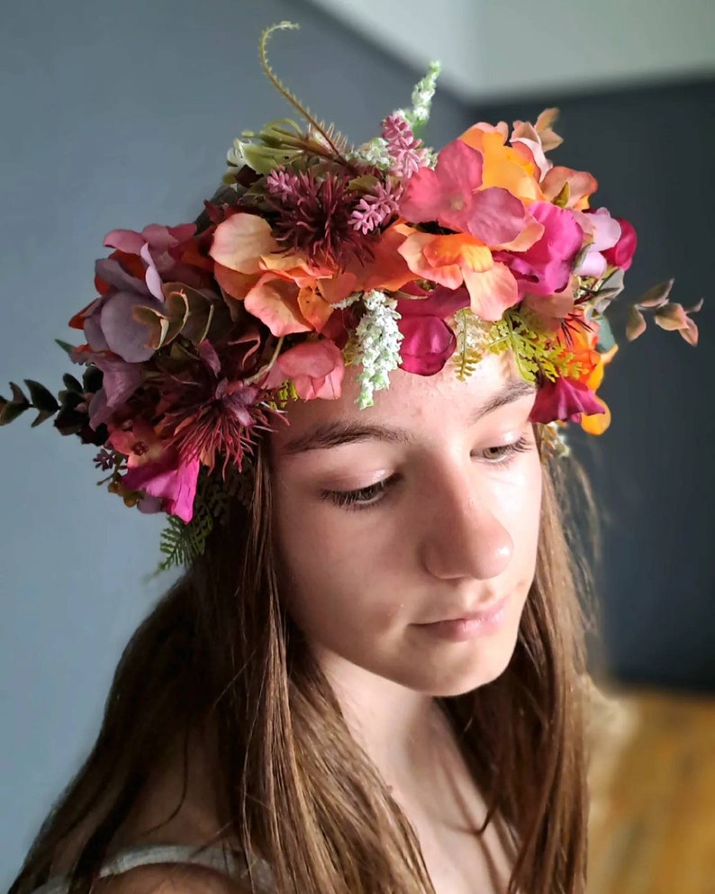 May include: A floral crown with pink, orange, and green flowers. The crown is worn on the head of a person with long brown hair.