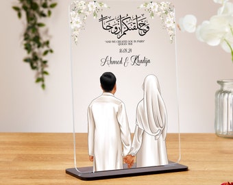 May include: A white acrylic plaque with a black floral design and Arabic calligraphy. The text reads "And We Created You In Pairs" Quran 78:8. Below the text is the date 16.08.24 and the names "Ahmed & Khadija". The plaque features a black stand and a white illustration of a couple holding hands.