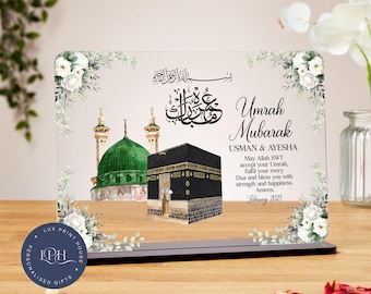 May include: A clear acrylic plaque with a floral design and an image of the Kaaba and the Green Dome. The text reads "Umrah Mubarak Usman & Ayesha May Allah SWT accept your Umrah, fulfil your every Dua and bless you with strength and happiness. Ameen. February 2025."