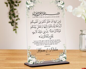 May include: A white acrylic plaque with a floral design and Arabic text. The text reads "In the name of Allah the most gracious and most merciful" and includes a verse from the Quran. The plaque also includes the names "Hasan & Alisha" and the date "16.05.24".