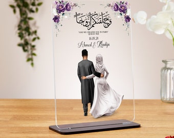 Op de afbeelding: Een heldere acrylplaat met een bloemenontwerp en een Arabische inscriptie. De plaat toont een stel in traditionele islamitische kleding, hand in hand lopend. De tekst luidt "En Wij hebben jullie in paren geschapen" (Koran 78:8) en bevat de datum "16.08.24" en de namen "Ahmed & Khadija".