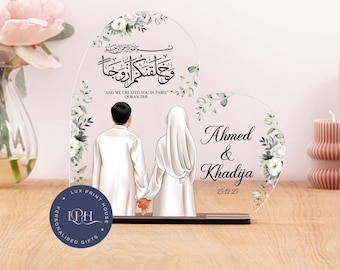 May include: A white acrylic heart-shaped stand with a floral design and a couple holding hands. The stand features Arabic calligraphy and the text "AND WE CREATED YOU IN PAIRS QURAN 78:8". The stand also includes the names "Ahmed & Khadija" and the date "25.12.25".