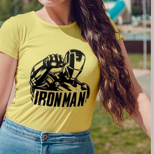 May include: Yellow t-shirt featuring a black and white graphic of Iron Man with the word "IRONMAN" below. The image also includes text indicating the availability of the design in AI, SVG, EPS, DXF, and PNG formats.