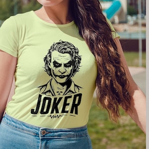 Puede incluir: Una camiseta amarilla clara con una ilustraci&oacute;n en blanco y negro del Joker de los c&oacute;mics de Batman. El texto "JOKER" est&aacute; impreso en negro debajo de la ilustraci&oacute;n.