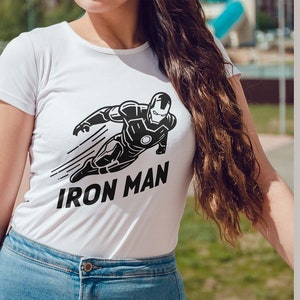 May include: White t-shirt featuring a black and white Iron Man graphic. The design shows Iron Man in a dynamic pose with the text "IRON MAN" below. The image also includes file type options: AI, SVG, EPS, DXF, and PNG.