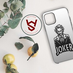 Puede incluir: Una funda de tel&eacute;fono blanca con una ilustraci&oacute;n en blanco y negro del Joker de Batman. El texto "JOKER" est&aacute; impreso en negro debajo de la ilustraci&oacute;n.
