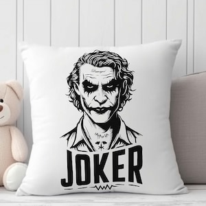 Puede incluir: Almohada blanca con una ilustraci&oacute;n en blanco y negro del Joker de Batman. El Joker est&aacute; representado con un traje y una sonrisa siniestra. El texto "JOKER" est&aacute; impreso debajo de la ilustraci&oacute;n.