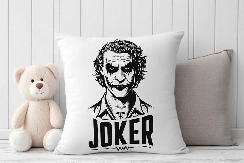 Puede incluir: Almohada blanca con una ilustraci&oacute;n en blanco y negro del Joker de Batman. El Joker est&aacute; representado con un traje y una sonrisa siniestra. El texto "JOKER" est&aacute; impreso debajo de la ilustraci&oacute;n.