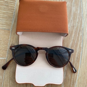 May include: A pair of tortoise shell sunglasses with a brown leather case. The case has a light pink lining.