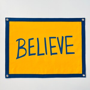 May include: A yellow fabric banner with a navy blue border and the word "BELIEVE" written in navy blue.