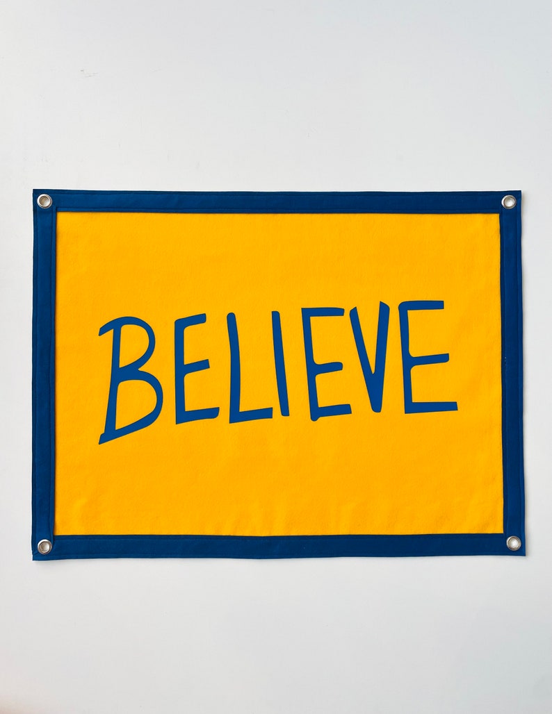 May include: A yellow fabric banner with a navy blue border and the word "BELIEVE" written in navy blue.