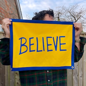 May include: A yellow banner with a blue border and the word "BELIEVE" written in blue.