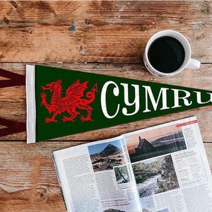 May include: A green pennant with a red dragon and the word "CYMRU" in white lettering. The pennant is on a wooden surface with a cup of coffee and a magazine.