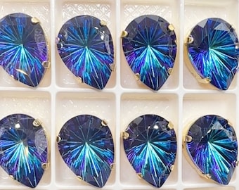 May include: Twelve pear-shaped iridescent blue rhinestones with gold settings are arranged in a grid pattern. The rhinestones have a starburst design.