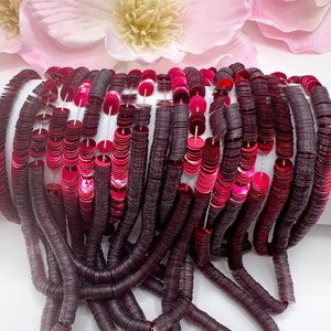 May include: A strand of dark burgundy and bright pink sequins, arranged in a cascading pattern. The sequins are small and round, and they are strung together on a clear thread.