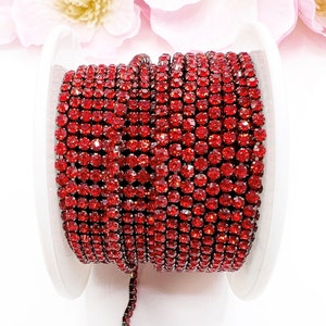 May include: A spool of red rhinestone chain trim. The chain is made of small, round rhinestones that are connected by silver metal.