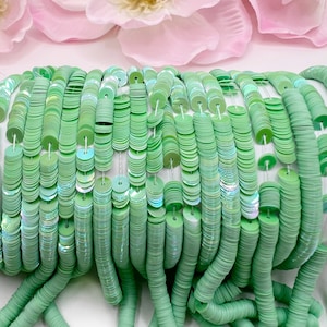 May include: A close-up of a strand of light green iridescent sequins. The sequins are strung together on a white thread and are arranged in a cascading pattern.