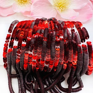 May include: A spool of red and burgundy sequins, with the sequins arranged in rows. The sequins are round and have a metallic sheen.