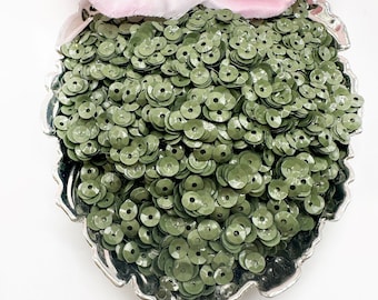 May include: A close-up of a silver bowl filled with green sequins. The sequins are round and have a slightly raised center.