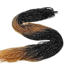 May include: A strand of black and gold glass beads. The beads are small and round, and they are arranged in a gradient from black to gold.