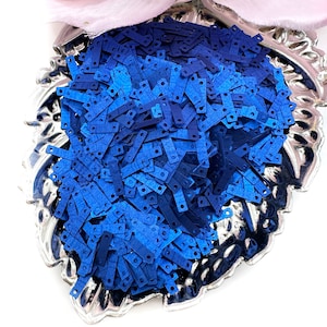 May include: A silver bowl filled with blue and dark blue iridescent sequins. The sequins are shaped like small rectangles with rounded corners.
