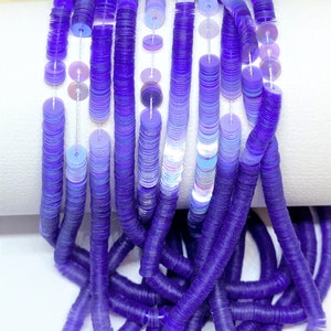 May include: A strand of iridescent purple and light blue sequins, strung on white thread. The sequins are round and flat, and they are arranged in a graduated pattern, with the purple sequins at the bottom and the light blue sequins at the top.