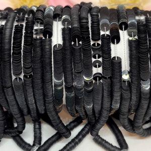 May include: A close-up of a strand of black sequins. The sequins are round and have a slight iridescent sheen. They are strung on a white thread.