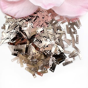 May include: A pile of silver and rose gold metal sequins with two holes in each. The sequins are rectangular and have a shiny finish.