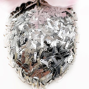 May include: A silver bowl filled with a large quantity of small, silver, rectangular sequins with two holes on each end.