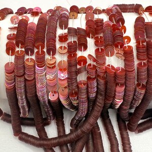 May include: A strand of iridescent red sequins, strung on white thread. The sequins are round and flat, with a slight shimmer.