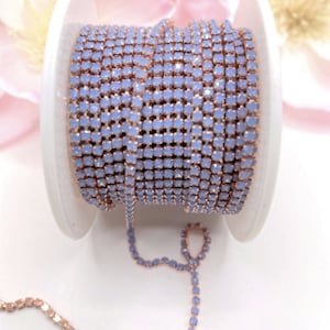 May include: A spool of light blue rhinestone chain with rose gold metal connectors. The chain is coiled on a white spool.