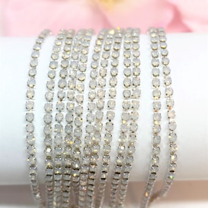 May include: A close-up of a silver chain with clear, iridescent rhinestones. The chain is made of small, round rhinestones that are connected by silver metal.