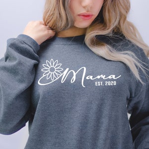 May include: A dark grey sweatshirt with a white daisy and the text "Mama Est. 2020" printed on the front.