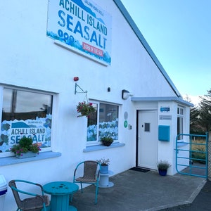 May include: A white ceramic mug with a black handle and the text "But first, coffee" in a handwritten style. The mug is designed for hot drinks and has a glossy finish.