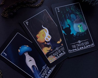 以下が含まれることがあります： 黒い縁取りと装飾的なデザインが施されたタロットカード3枚。カードは「カップの騎士」、「カップのペイジ」、「ジオの2」です。