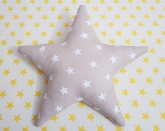 May include: A beige star-shaped pillow with white star patterns. The pillow is on a yellow background with repeating yellow star patterns. The pillow is a decorative item.