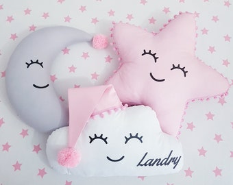 May include: Three plush pillows shaped like a moon, a star, and a cloud. The pillows have embroidered eyes, smiles, and eyelashes. The cloud pillow has the name "Landry" embroidered on it.