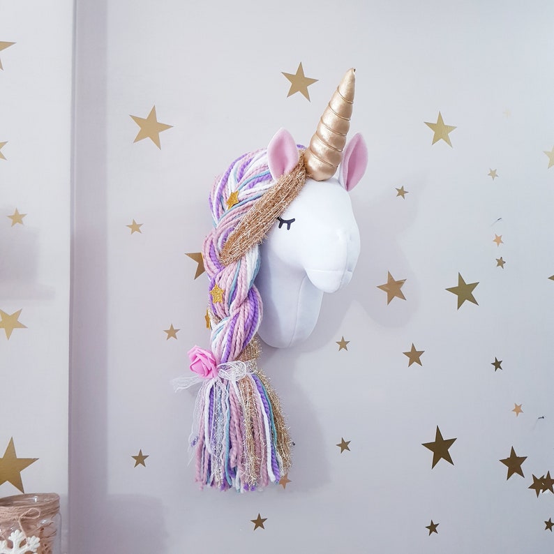 May include: A white unicorn head wall decoration featuring a gold horn and pink ears. The unicorn has a long, braided mane in shades of purple, blue, and gold, decorated with gold stars and a pink flower. The wall is decorated with gold star stickers.
