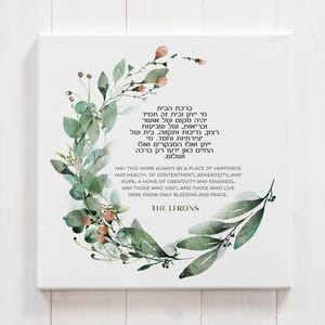 May include: A square canvas print featuring a watercolor wreath of green leaves and small orange flowers. The center contains Hebrew text and the English inscription: May this home always be a place of happiness and health, of contentment, generosity, and hope, a home of creativity and kindness. May those who visit, and those who live here know only blessing and peace. The Efrons.