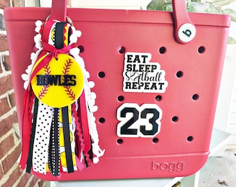 May include: A red and white  Bogg bag with a black and white softball charm, a black and white sticker that says "Eat Sleep Softball Repeat", and a black and white number 23 sticker.
