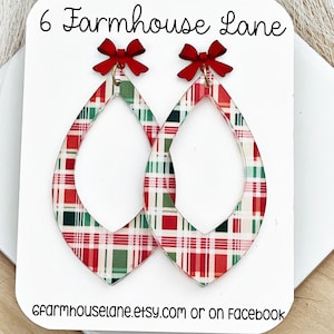 May include: Teardrop-shaped earrings featuring a red, green, and white plaid pattern. Each earring is topped with a small red bow. The earrings are displayed on a white card labeled 6 Farmhouse Lane and 6farmhouselane.etsy.com or on facebook.