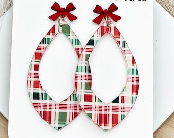 May include: Teardrop-shaped earrings featuring a red, green, and white plaid pattern. Each earring is topped with a small red bow. The earrings are displayed on a white card labeled 6 Farmhouse Lane and 6farmhouselane.etsy.com or on facebook.