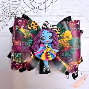 May include: A colorful hair bow with a patchwork design featuring a character from the Nightmare Before Christmas. The character is a girl with purple hair, a blue dress, and a black bow. The bow is decorated with black and white stripes and a black and white smiley face.