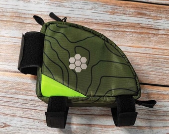 Op de afbeelding: Een groene en zwarte fietssaddlebag met een honingraatpatroon en een reflecterende groene streep. De tas heeft verstelbare banden om aan een fietszadel te bevestigen.