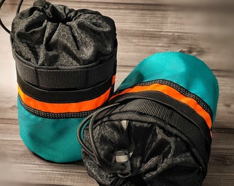 Op de afbeelding: Twee teal en zwarte cilindrische tassen met oranje afwerking en trekkoorden. De tassen zijn gemaakt van waterbestendig materiaal en hebben een honingraatpatroon.