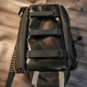 May include: Black bicycle pannier bag with reflective stripes and adjustable straps. The bag is made of a durable, waterproof material and features multiple compartments for storage. The bag is designed to attach to a bicycle rack for easy transport of items.