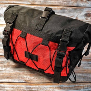 Op de afbeelding: Zwarte en rode fietstas voor het stuur met verstelbare banden en een mesh-vak. De tas heeft een trekkoord sluiting en een reflecterende strip.