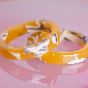 Può includere: Due anelli in resina gialla con un motivo a marmo bianco e nero.