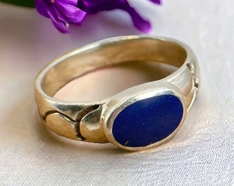 Può includere: Un anello d'argento con una pietra ovale blu incastonata in una fascia decorativa.