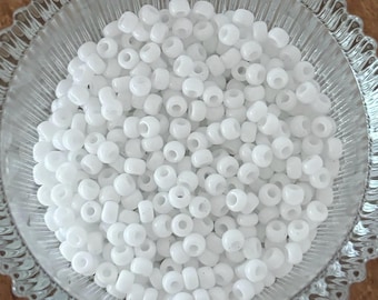 May include: A bowl filled with white opaque round seed beads. The beads are small and uniform in size.